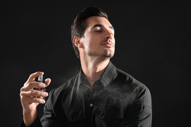 Handsome young man applying perfume on black background