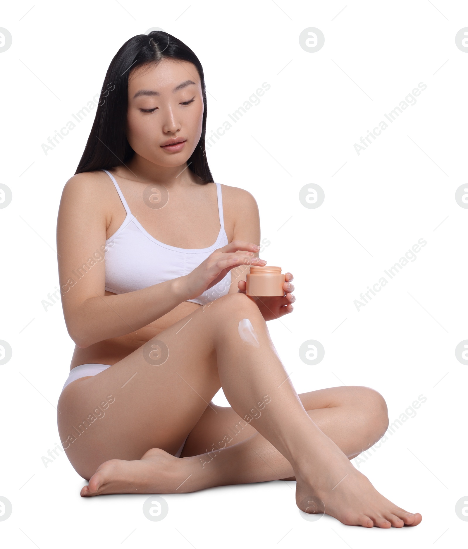 Photo of Beautiful young Asian woman applying body cream onto leg on white background