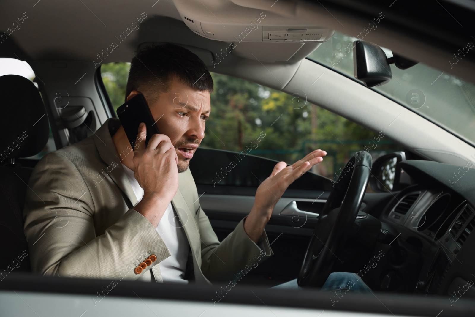 Photo of Stressed businessman talking on phone in driver's seat of modern car
