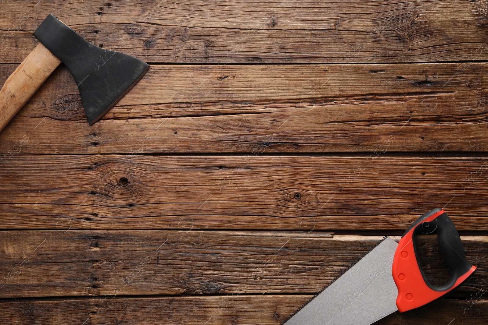 Photo of Saw with colorful handle and axe on wooden background, flat lay. Space for text