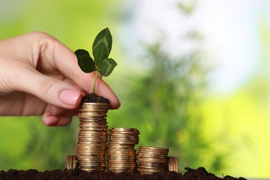 Photo of Woman putting coin with green sprout onto stack on soil against blurred background, closeup. Investment concept