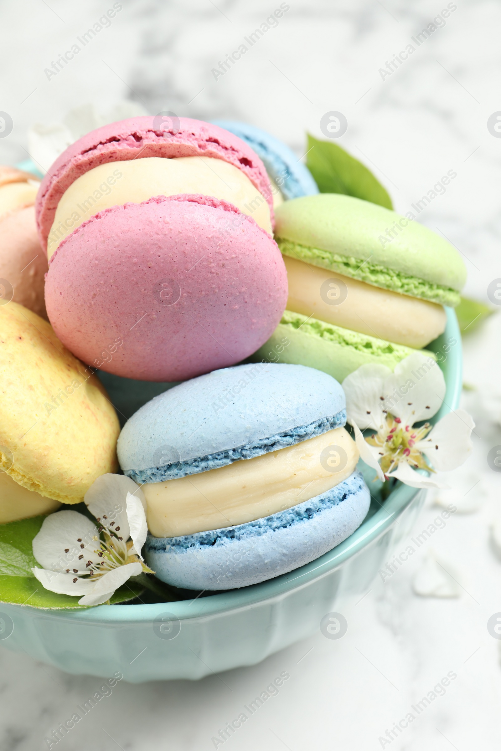 Photo of Delicious colorful macarons and flowers in bowl on white table, closeup