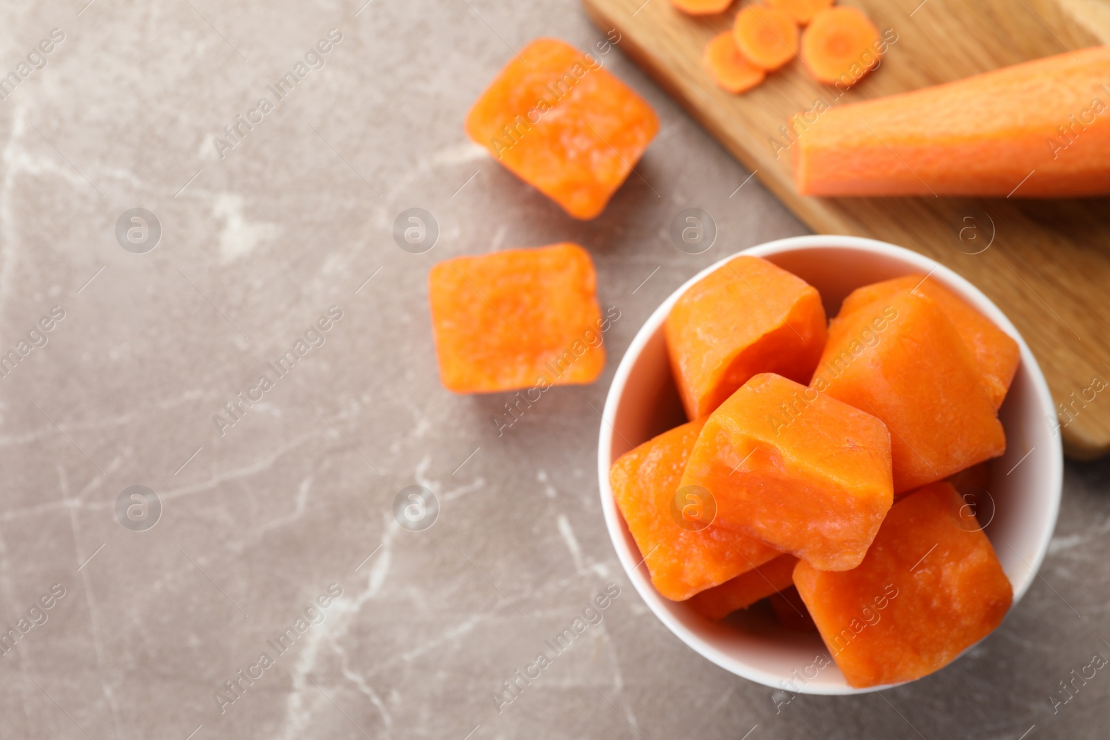 Photo of Bowl of frozen carrot puree cubes and ingredient on marble table, flat lay. Space for text