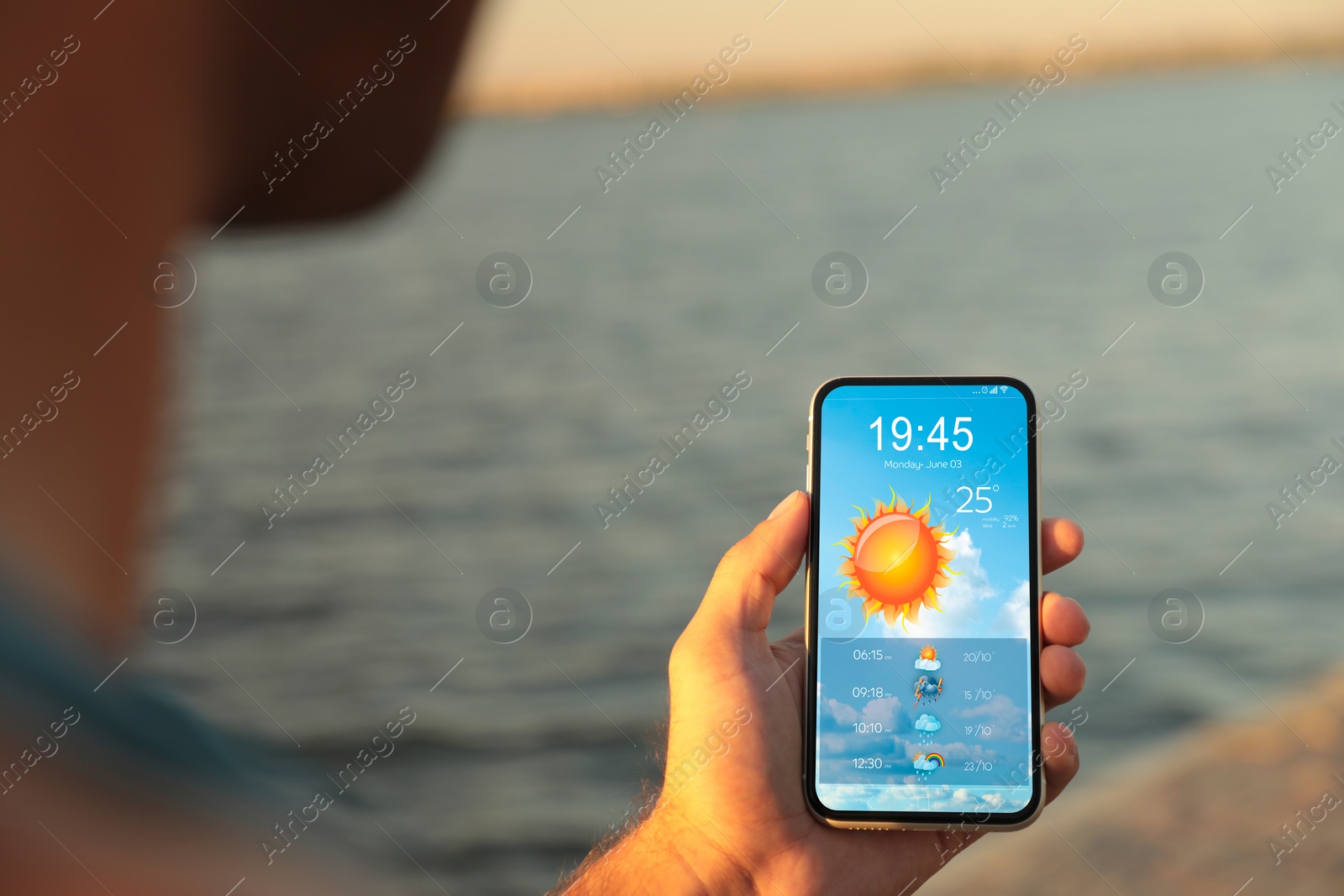 Image of Man checking weather using app on smartphone near river, closeup. Data, sun and other illustrations on screen