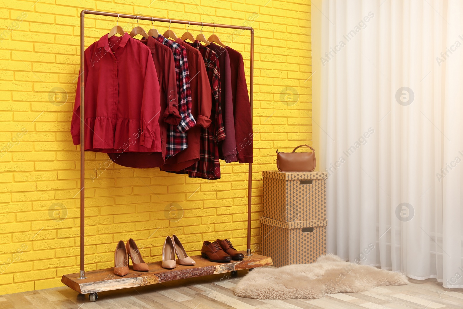 Photo of Rack with stylish clothes near yellow brick wall indoors