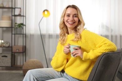 Photo of Happy woman in stylish warm sweater holding cup of drink at home. Space for text
