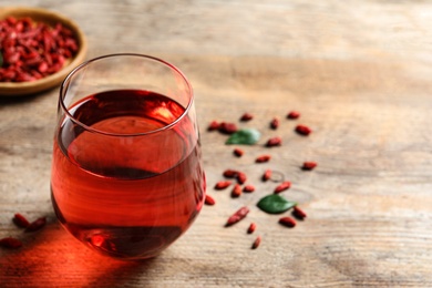 Photo of Glass of healthy goji juice on wooden table. Space for text