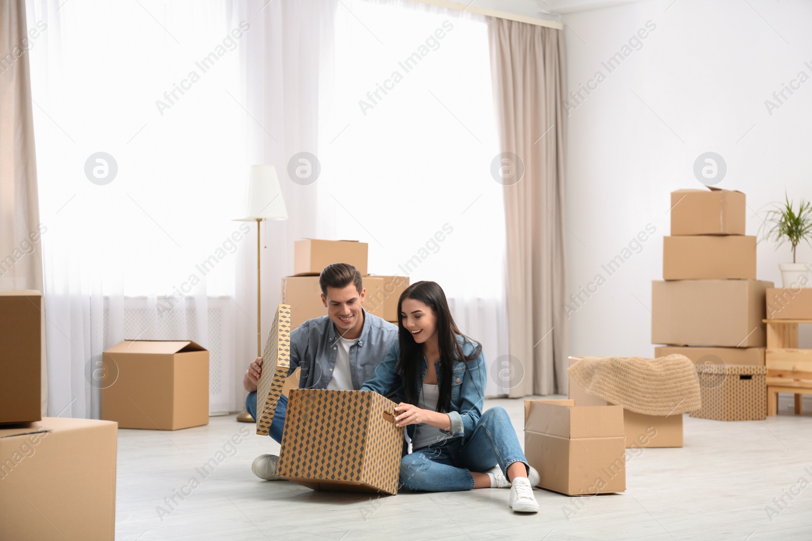 Photo of Happy couple unpacking cardboard boxes in their new flat on moving day