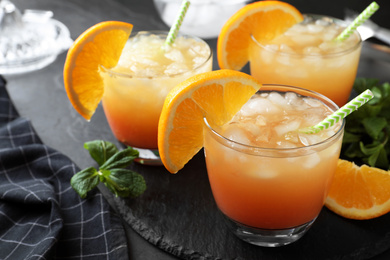 Photo of Glasses of tasty tropical cocktail on black table