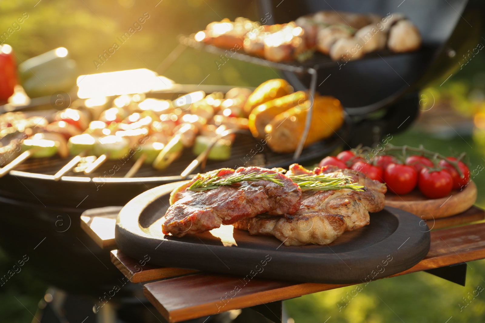 Photo of Tasty cooked meat and cherry tomatoes on table near barbecue grill outdoors