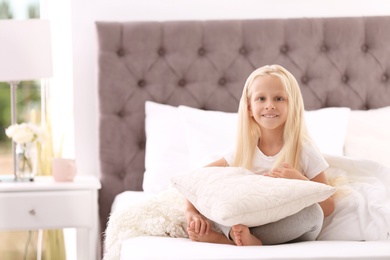 Photo of Cute little girl with pillow sitting on bed at home