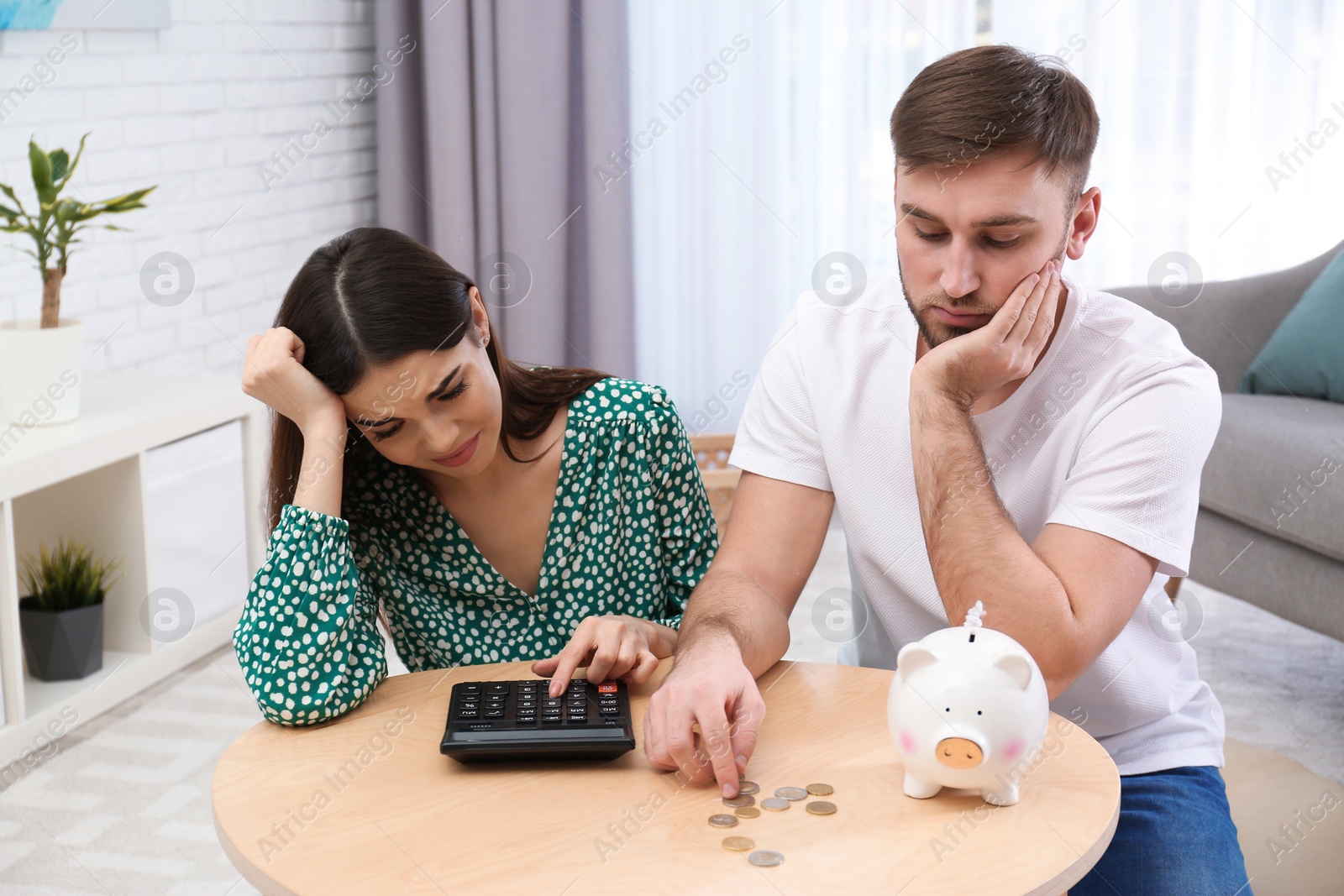 Photo of Unhappy young couple with piggy bank and money at home. Financial problems