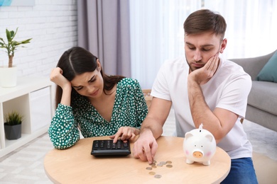 Unhappy young couple with piggy bank and money at home. Financial problems