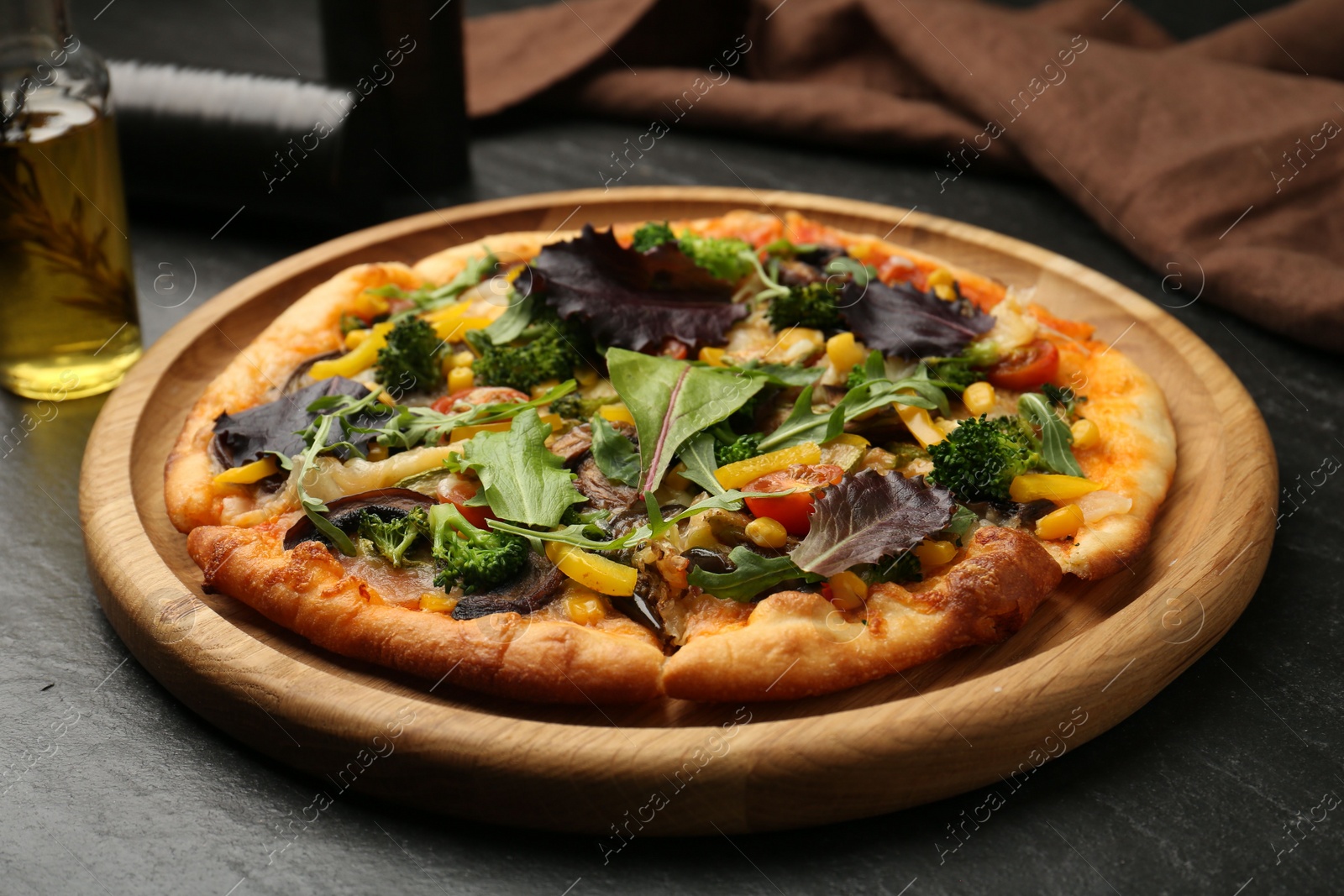 Photo of Delicious vegetarian pizza with vegetables and greens on black table