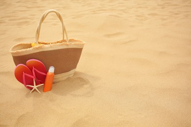 Straw bag, flip flops, starfish and sunscreen on sand, space for text