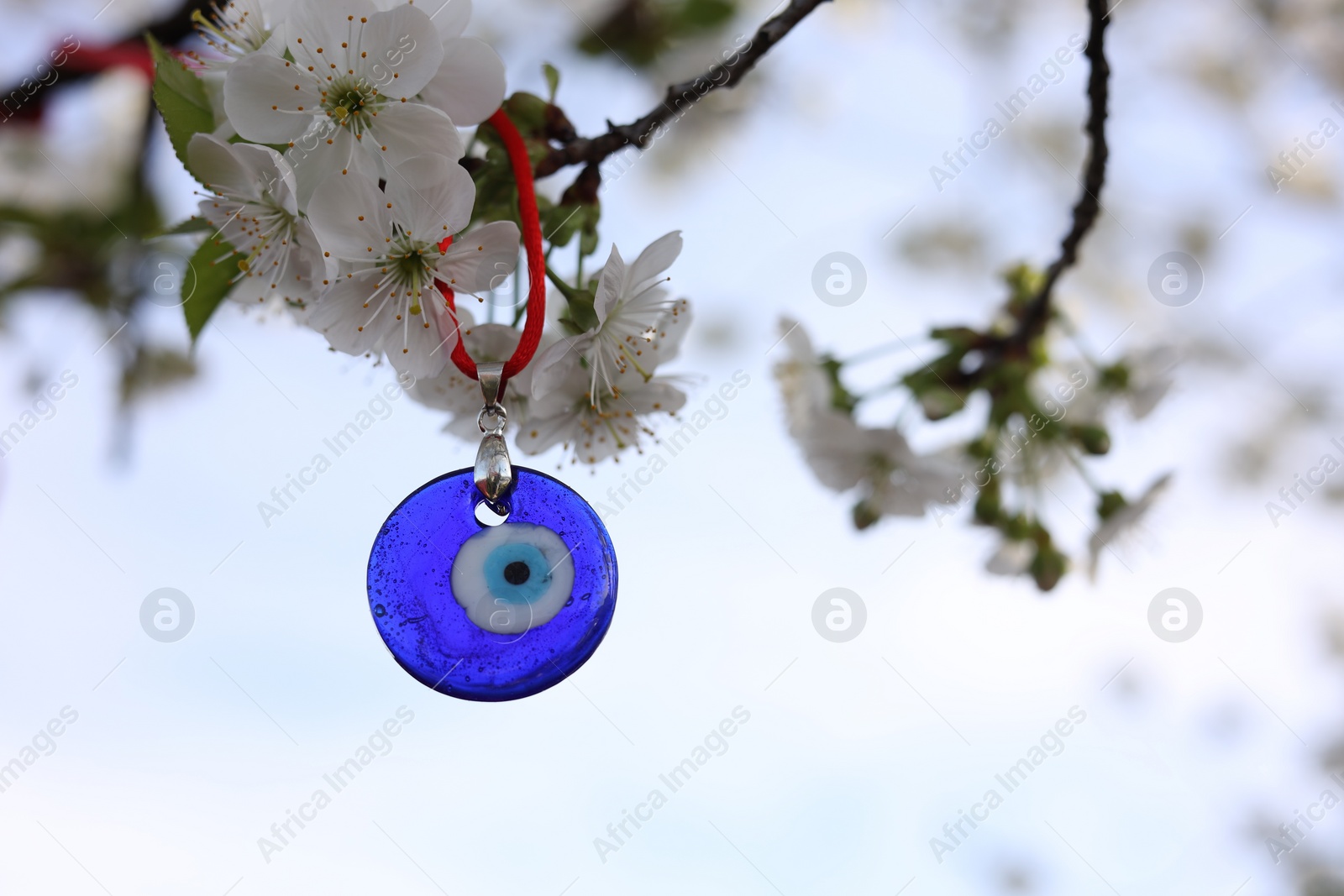 Photo of Evil eye amulet hanging on blossoming spring tree outdoors. Space for text