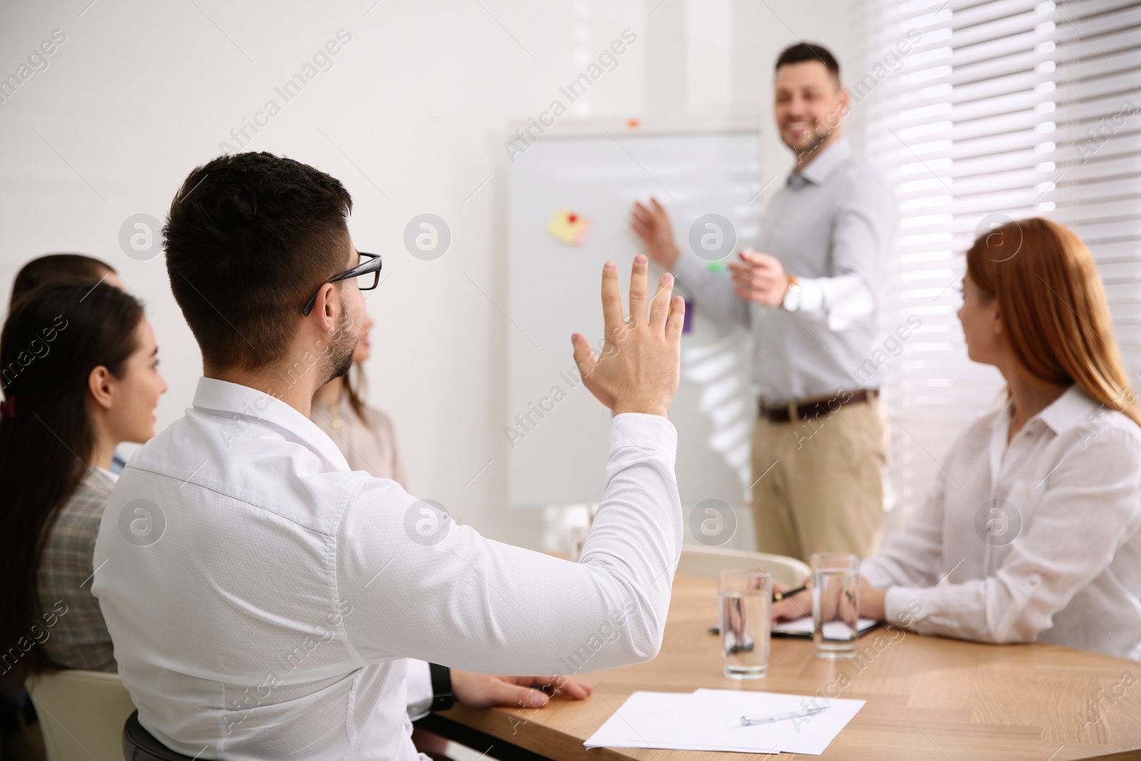 Photo of Young man raising hand to ask question at business training in conference room