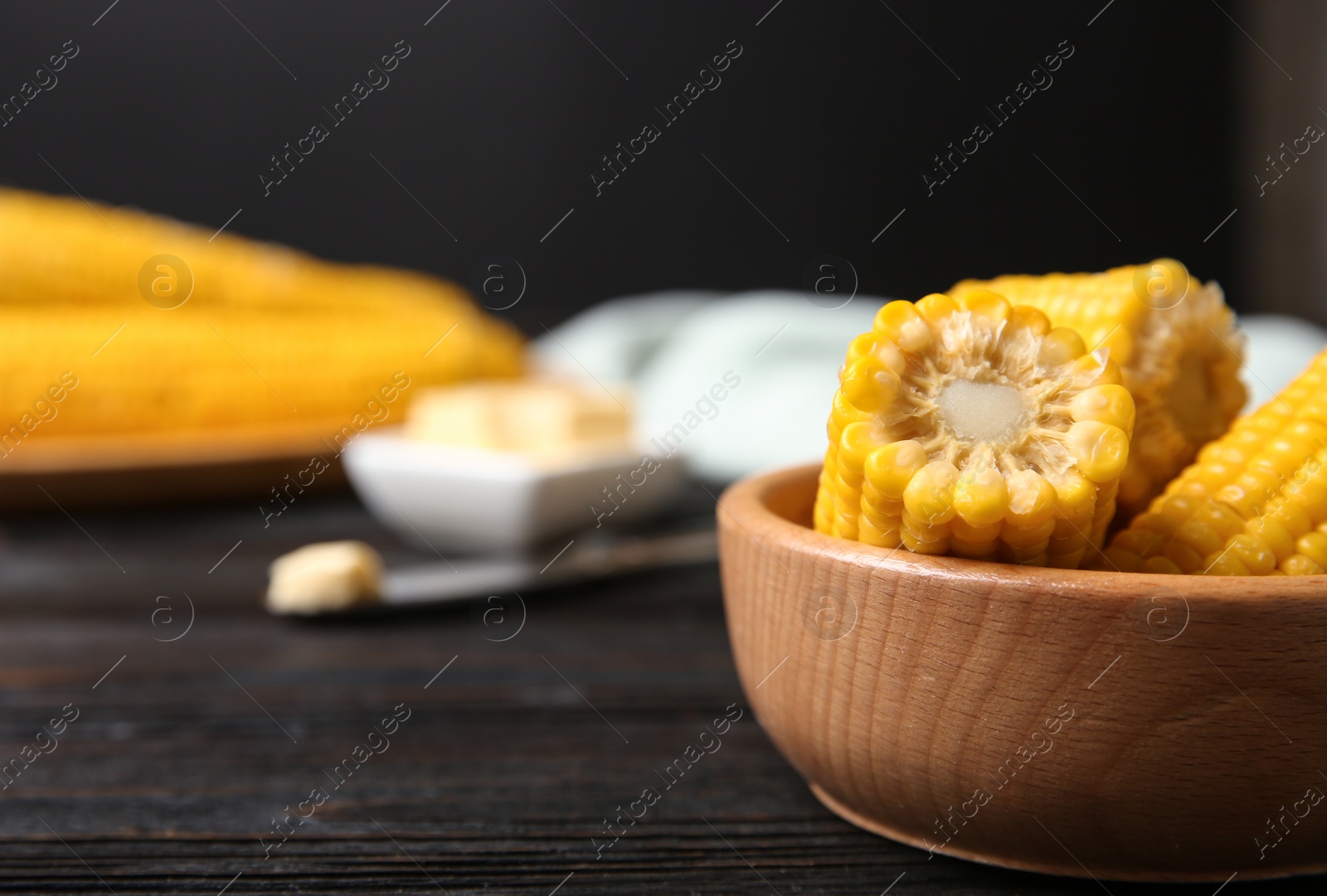 Photo of Wooden bowl of boiled corn cobs on black table, closeup. Space for text