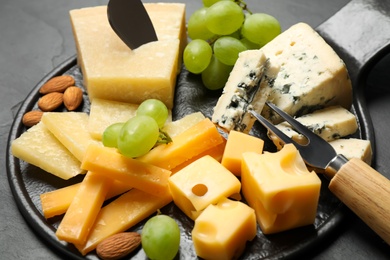 Photo of Cheese platter with specialized knife and fork on black table, closeup view