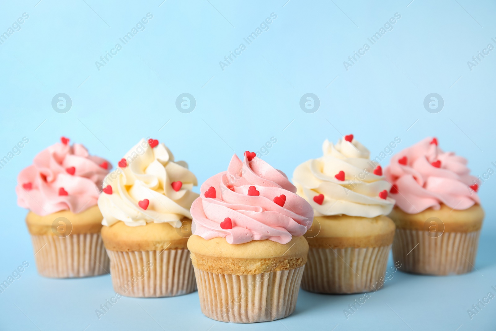 Photo of Tasty cupcakes with heart shaped sprinkles on light blue background. Valentine's Day celebration