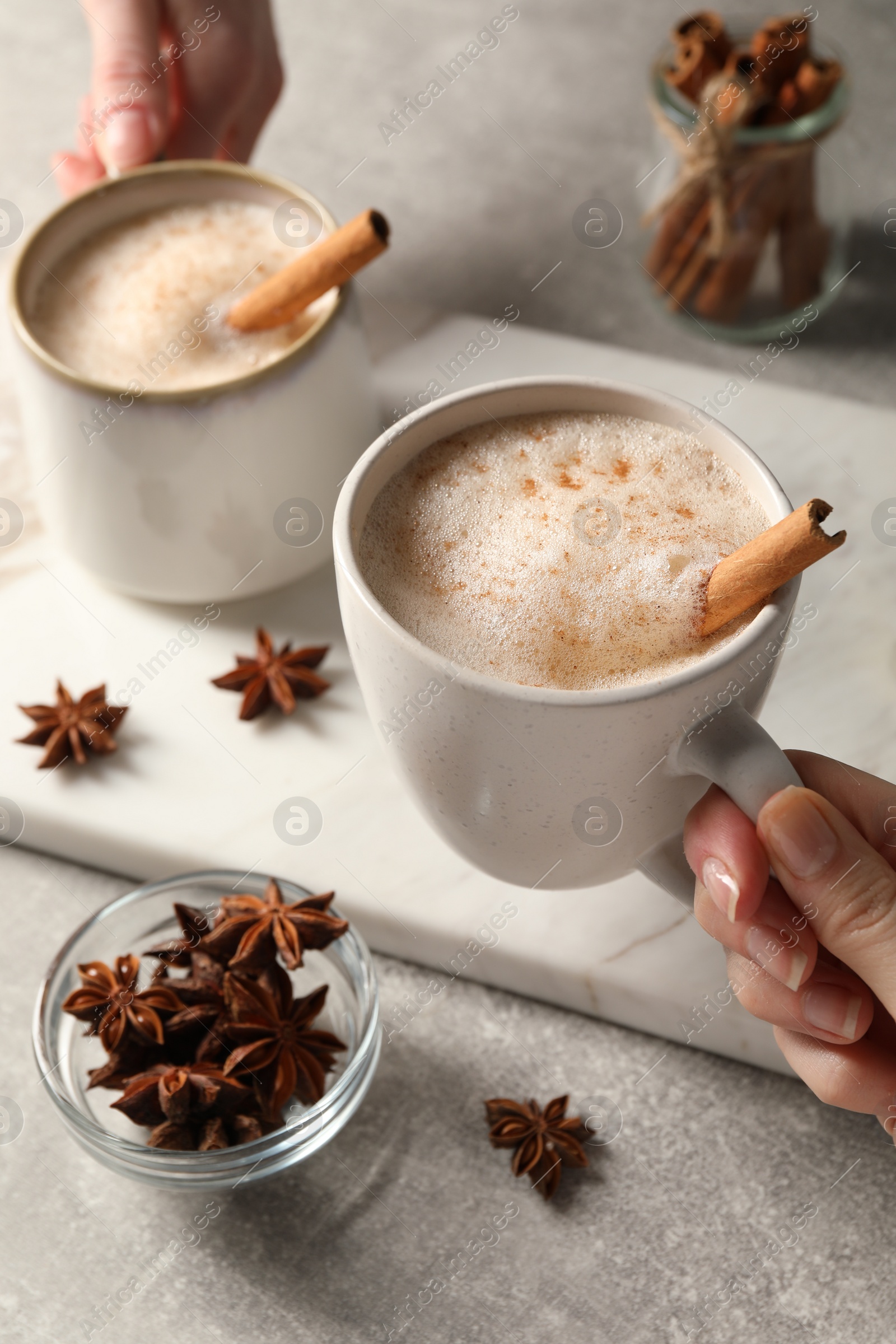 Photo of Women holding glass cups of delicious eggnog with cinnamon and anise at light grey table, closeup