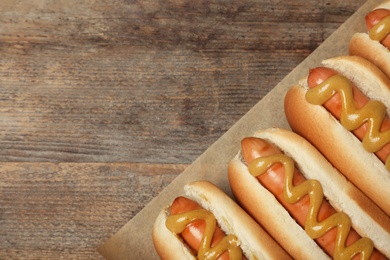 Hot dogs with mustard and space for text on wooden background, top view