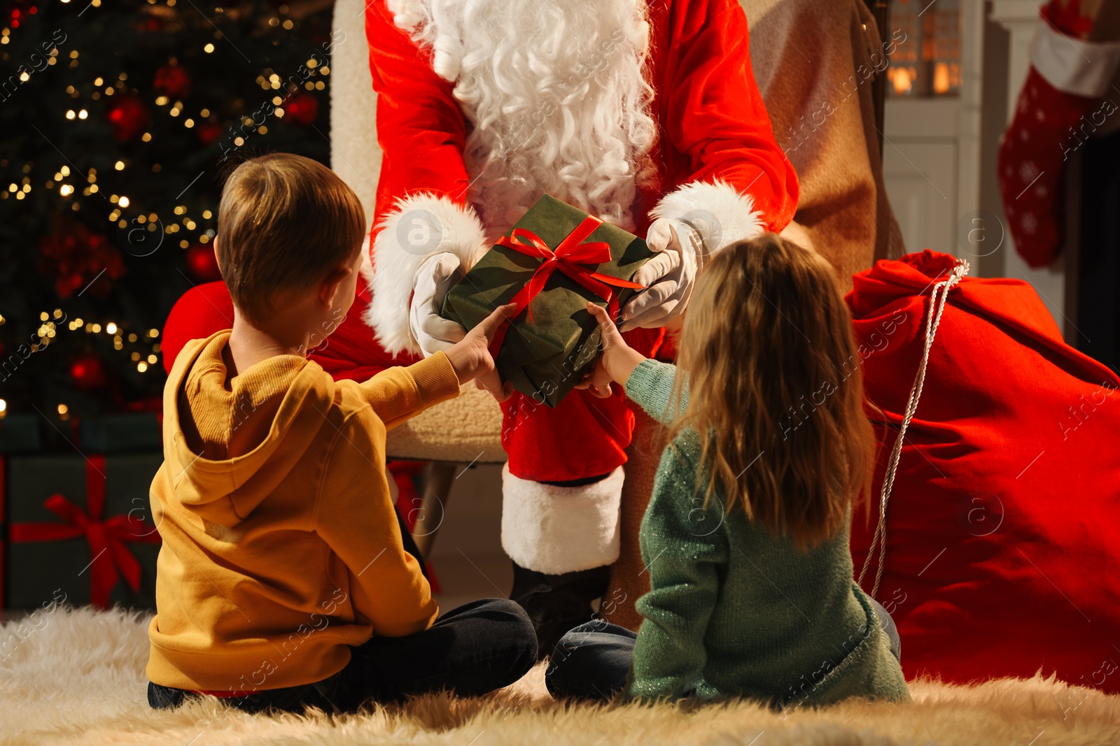 Photo of Santa Claus giving present to children in room with Christmas tree