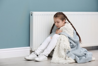 Sad little girl suffering from cold on floor near radiator