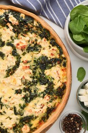 Delicious homemade spinach quiche and ingredients on white table, flat lay