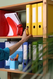 Photo of Woman taking binder office folder from shelving unit indoors, closeup