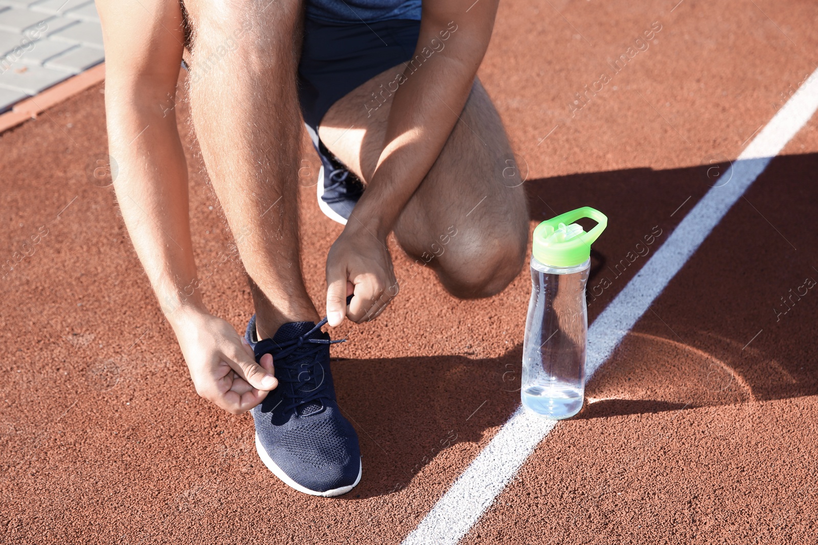 Photo of Sporty man tying shoelaces before running at stadium on sunny morning