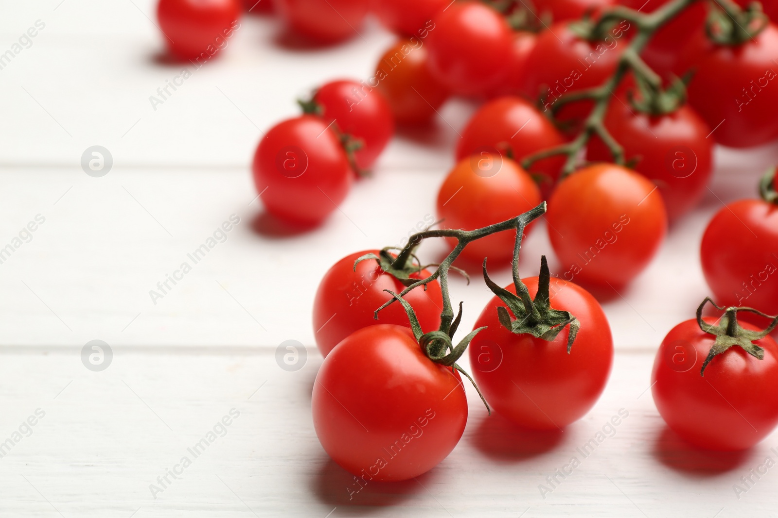 Photo of Fresh ripe cherry tomatoes on white wooden table, closeup. Space for text