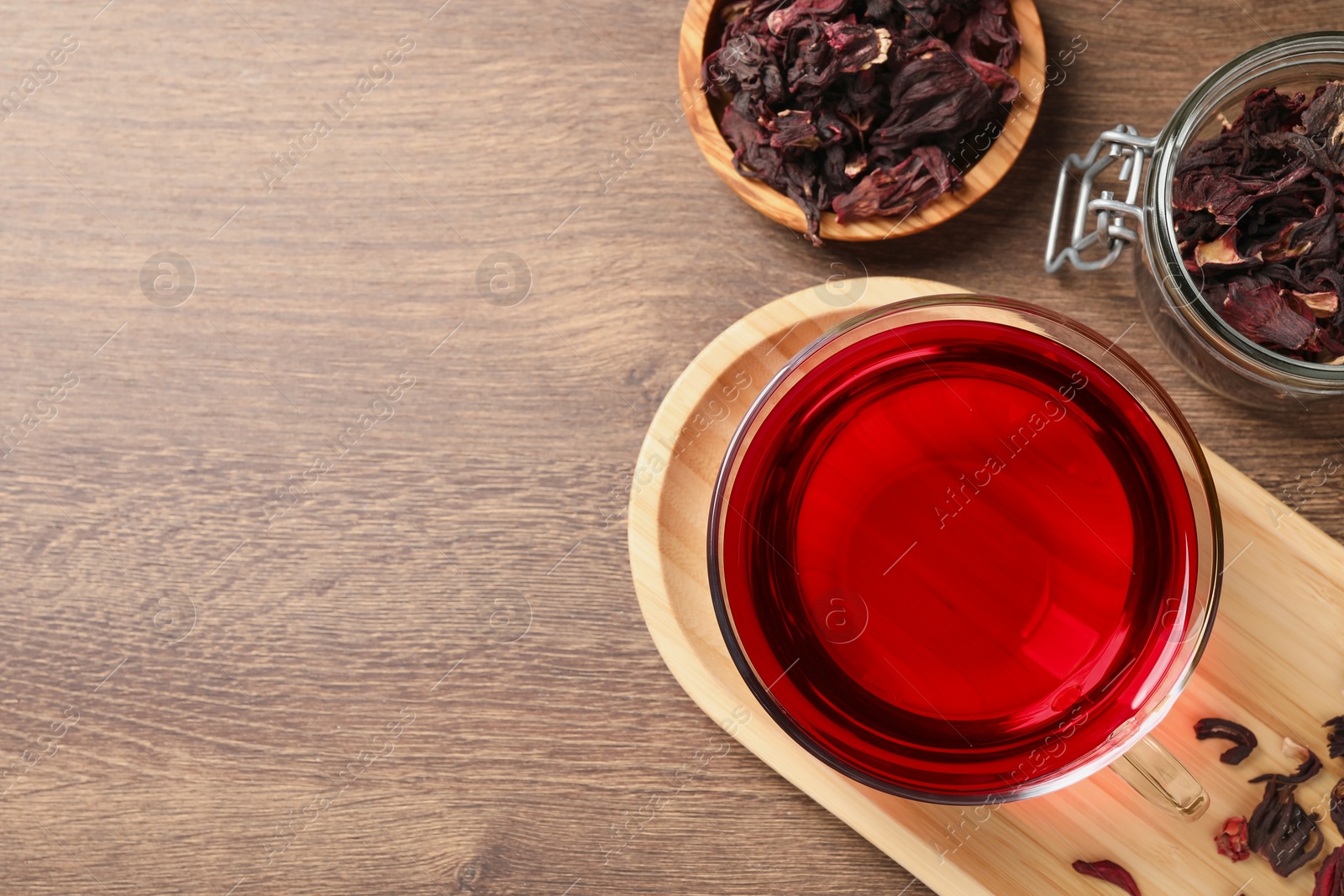 Photo of Cup of fresh hibiscus tea and dry flower leaves on wooden table, flat lay. Space for text