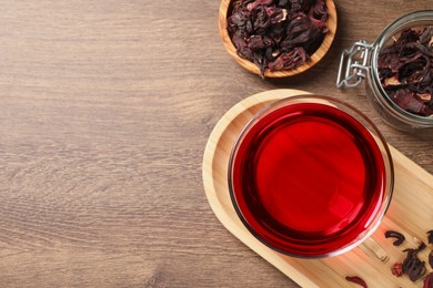 Photo of Cup of fresh hibiscus tea and dry flower leaves on wooden table, flat lay. Space for text