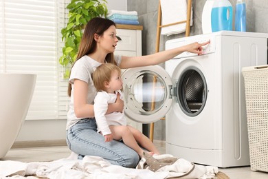 Mother with her daughter washing baby clothes in bathroom