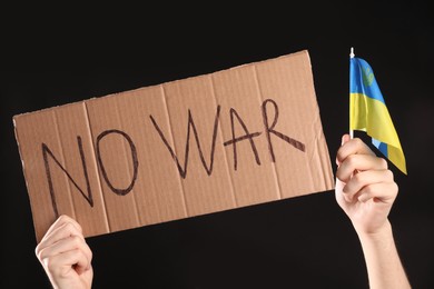 Photo of Teenage boy holding poster No War and Ukrainian flag against black background, closeup