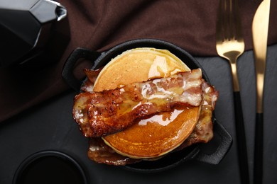 Photo of Delicious pancakes with maple syrup and fried bacon on black table, flat lay