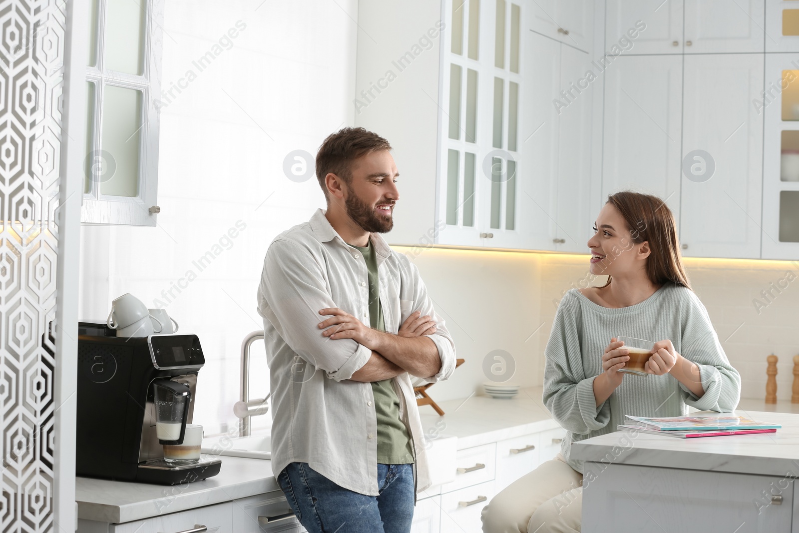 Photo of Young man talking with his girlfriend while using modern coffee machine in kitchen