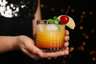 Woman with glass of Tequila Sunrise on blurred background, closeup. Delicious alcoholic cocktail