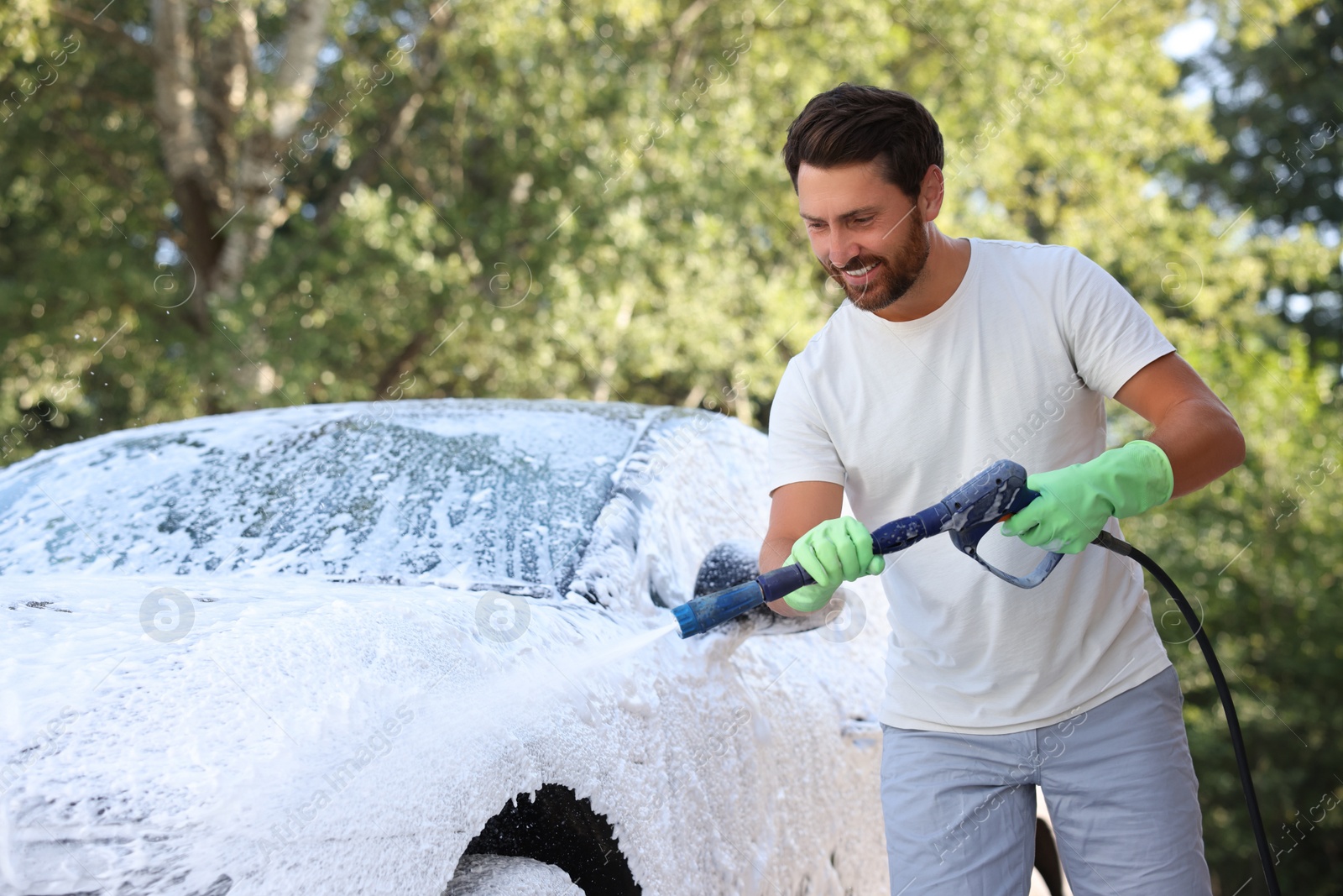 Photo of Man covering automobile with foam at outdoor car wash