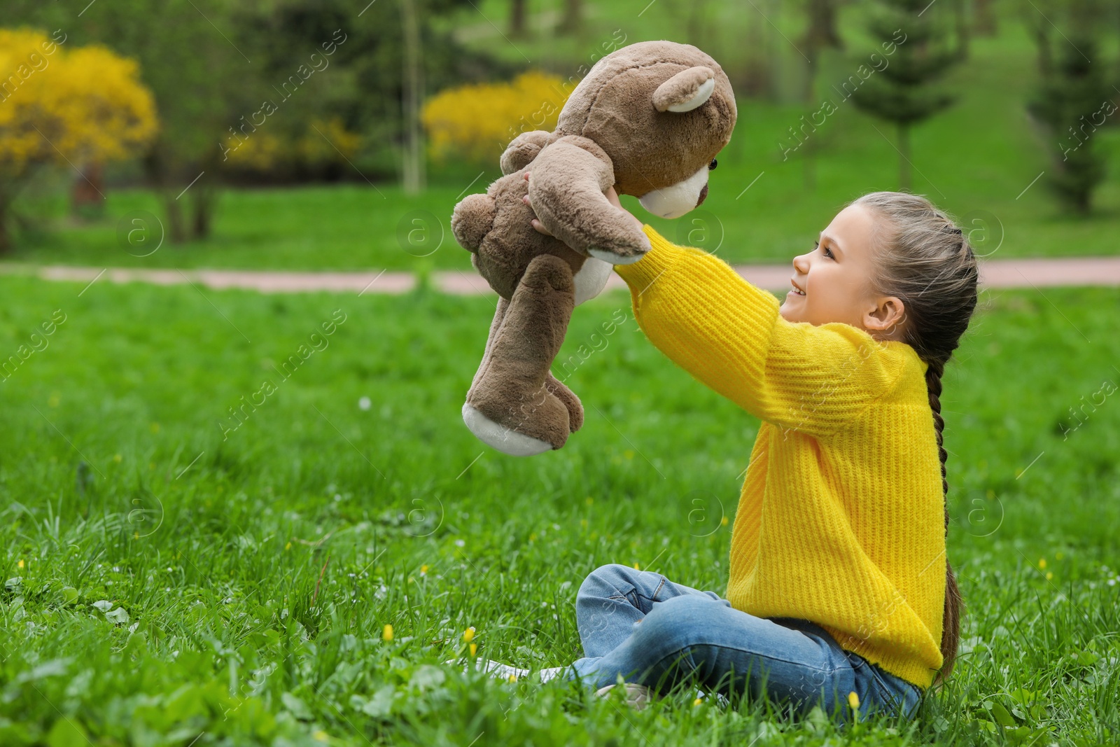 Photo of Little girl with teddy bear on green grass outdoors. Space for text