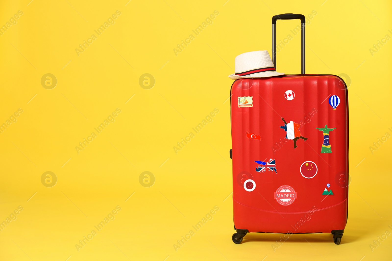 Image of Red suitcase with travel stickers on yellow background. Space for text