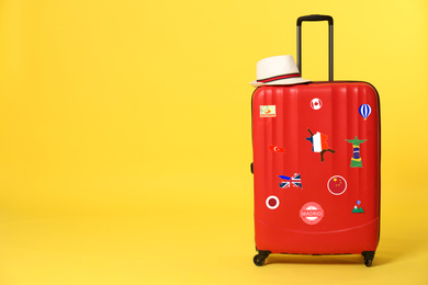 Image of Red suitcase with travel stickers on yellow background. Space for text