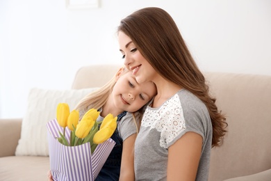 Photo of Cute little girl and her mother with tulip bouquet at home