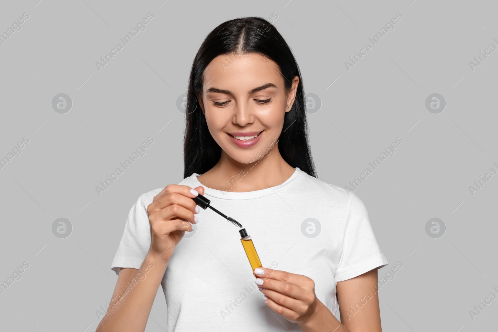 Photo of Young woman with eyelash oil on light grey background