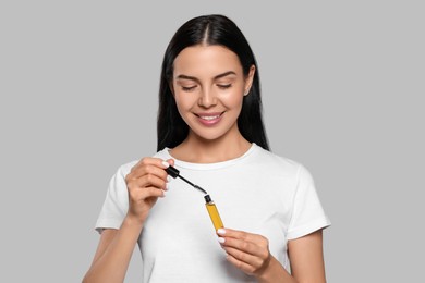 Young woman with eyelash oil on light grey background