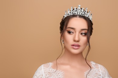 Beautiful young woman wearing luxurious tiara on beige background, space for text