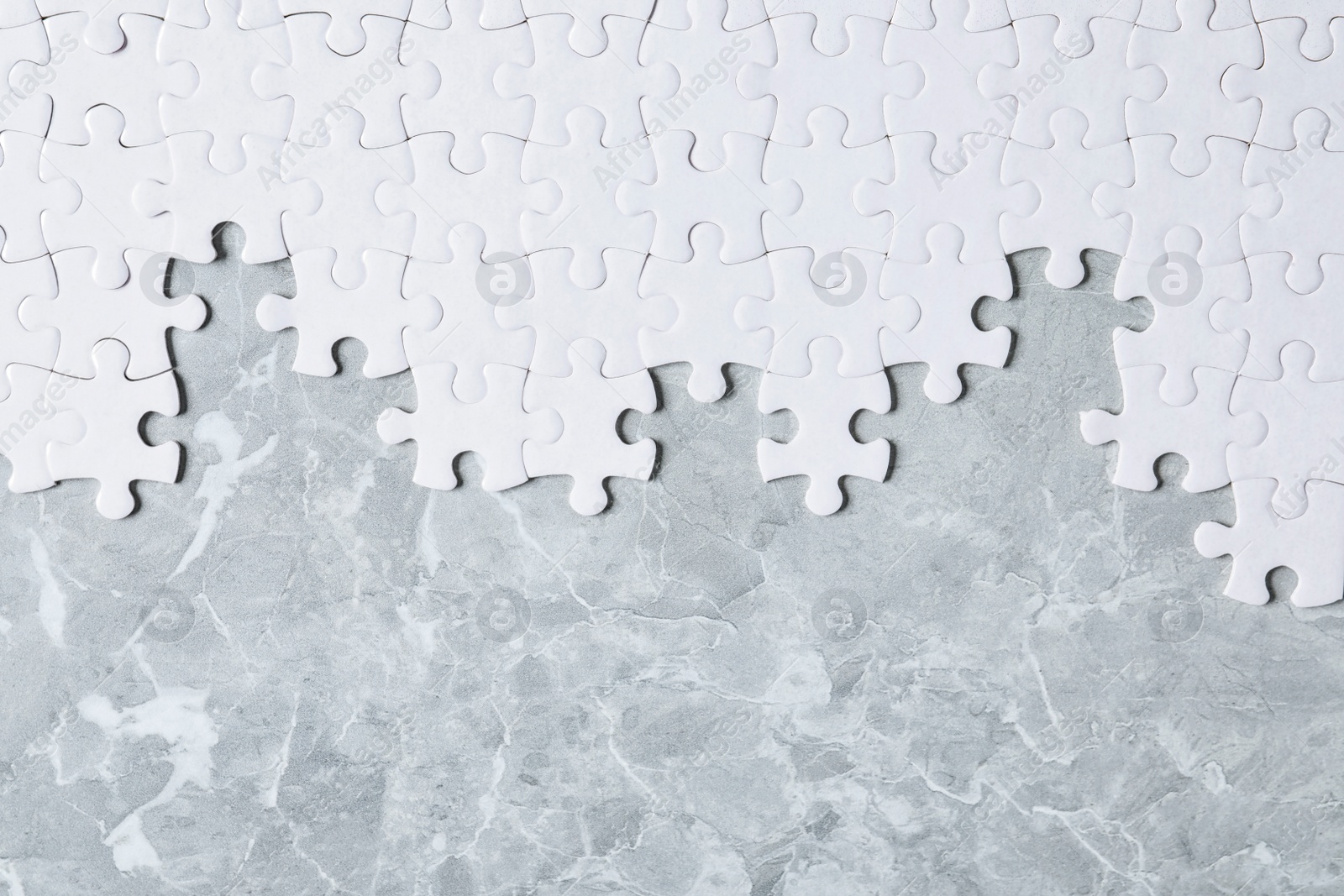 Photo of Blank white puzzle pieces on light grey marble background, flat lay. Space for text