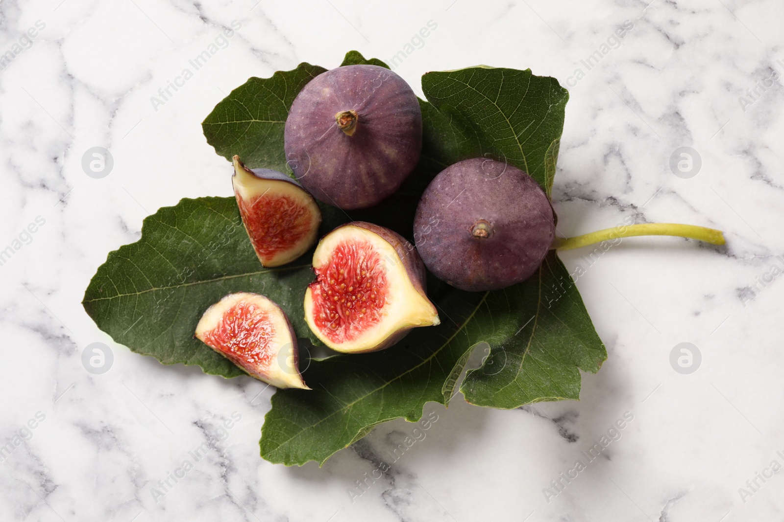 Photo of Whole and cut tasty fresh figs with green leaf on white marble table, flat lay