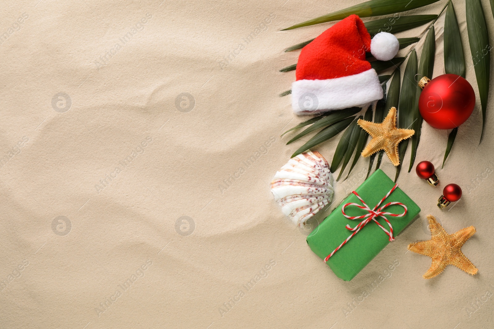 Photo of Flat lay composition with Santa hat and starfishes on sand, space for text. Christmas vacation